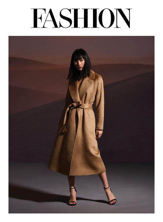 Image features the Fashion logo and an image of a female model wearing the Sentaler Suri Alpaca Long Notched Collar Raglan Sleeve Wrap Coat featured in Suri Alpaca and available in Dark Camel. Seen from front belted.