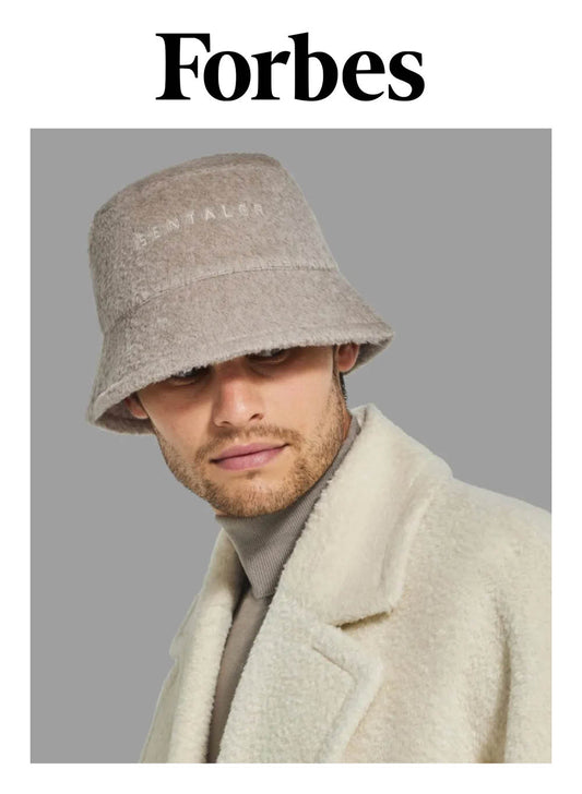 Image features the Forbes logo and an image of a male model wearing the Sentaler Mens Bouclé Alpaca Bucket Hat featured in Bouclé Alpaca and available in Sand Neutral. Seen close up from front.