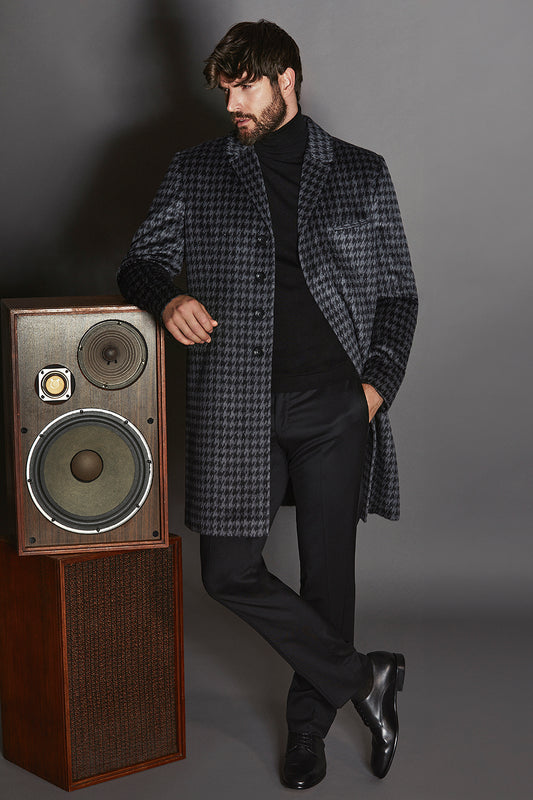 Sentaler Suri Alpaca Notched Lapel Black & Graphite Houndstooth Overcoat in Technical Suri Alpaca wool. Seen from front open on male model posing against retro speakers.