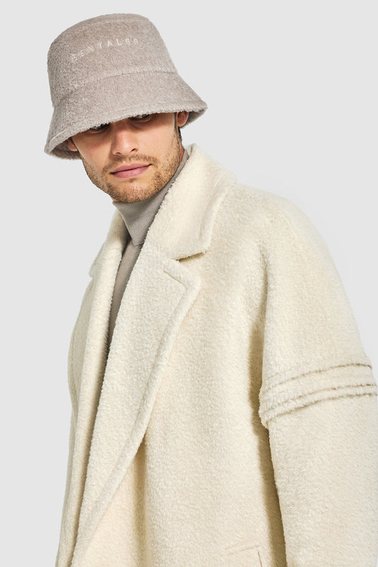 Sentaler Mens Bouclé Alpaca Bucket Hat featured in Bouclé Alpaca and available in Sand. Seen from front above waist on model.